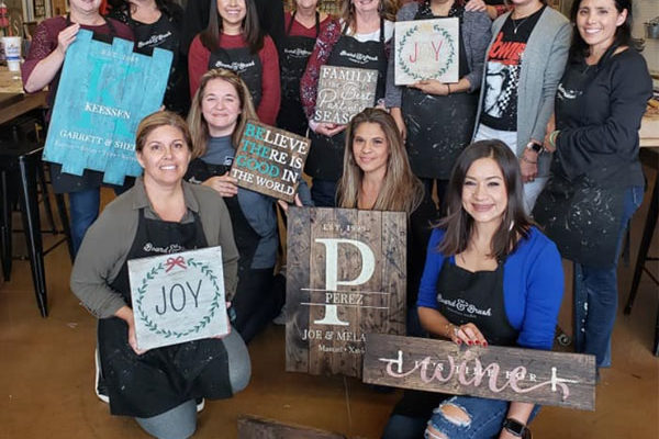 customers posing at Board-&-Brush with signs